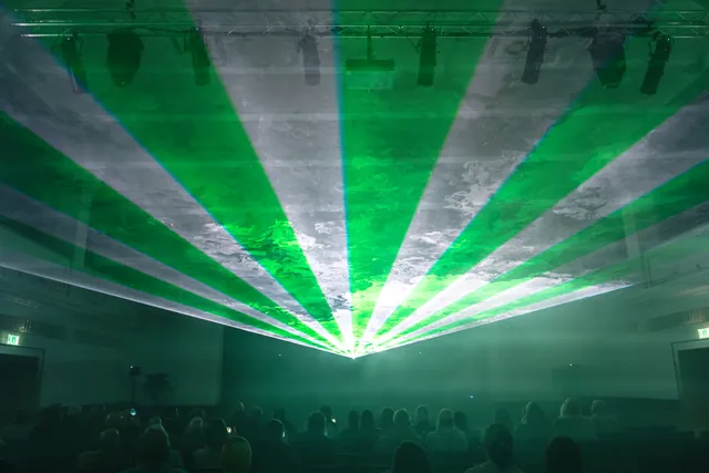 Laserstrahlen verlaufen hoch über dem Publikum in einem Saal